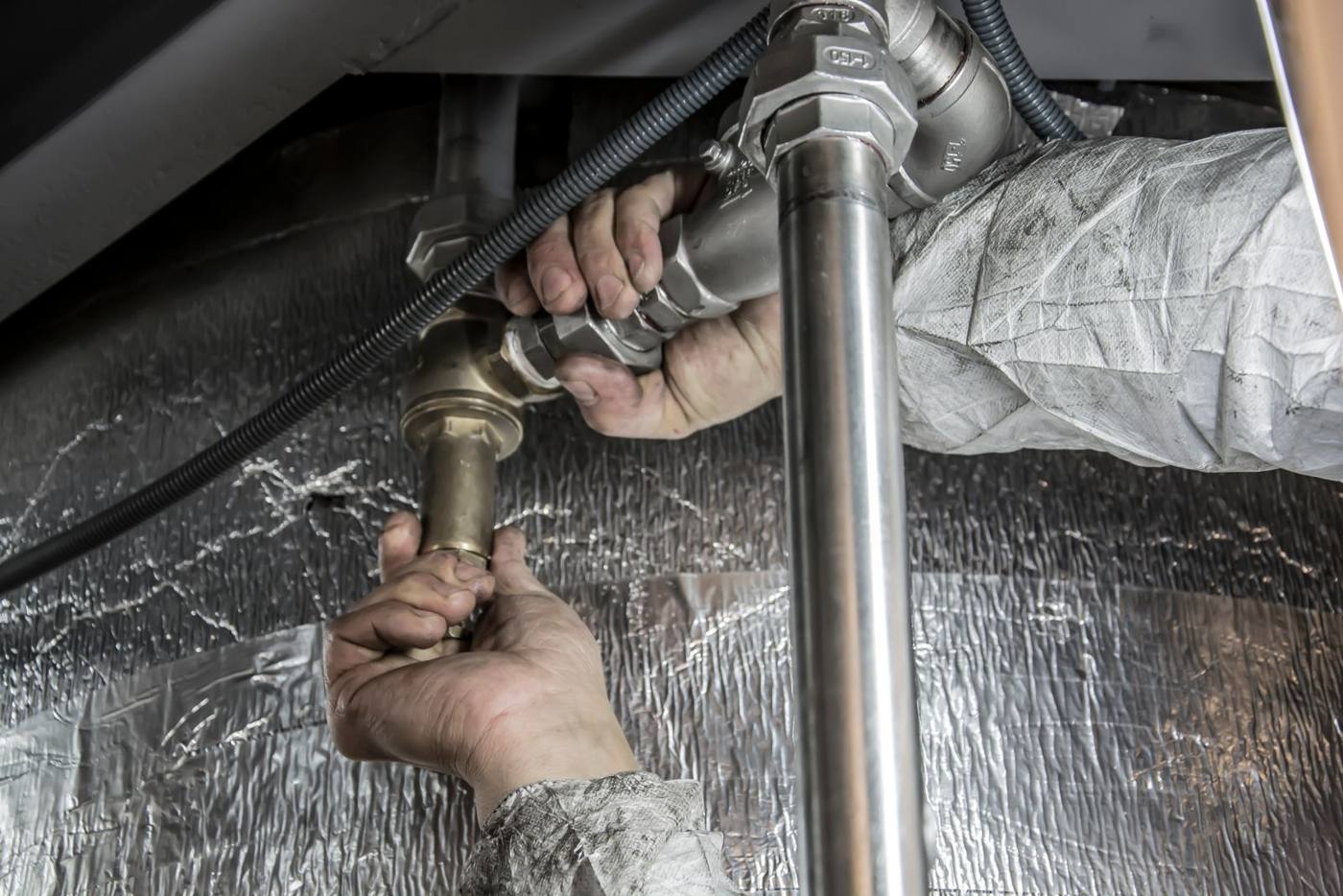 A plumber's hands tightening a fitting on a water line in a crawlspace