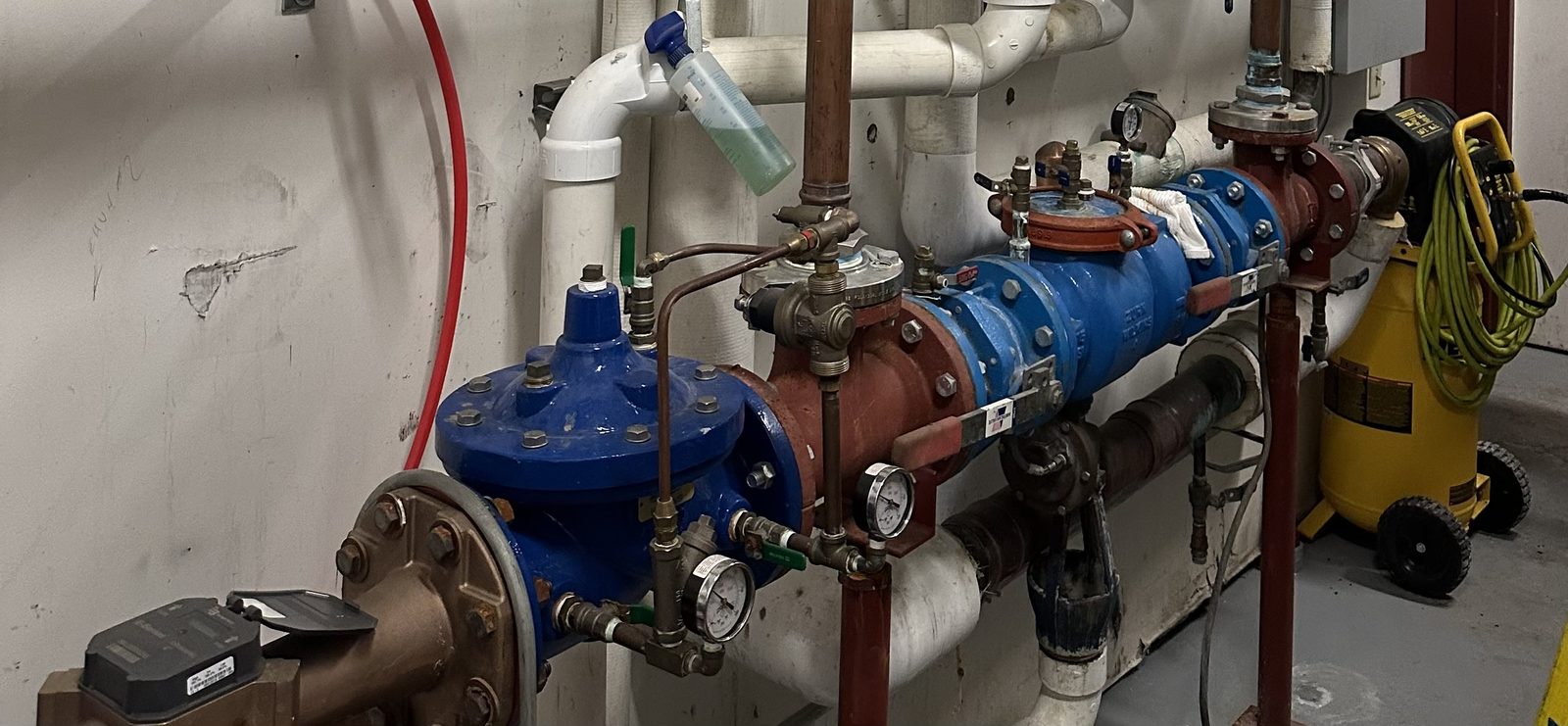 A large blue and red backflow preventer assembly with pressure gauges, installed on a commercial mechanical room wall