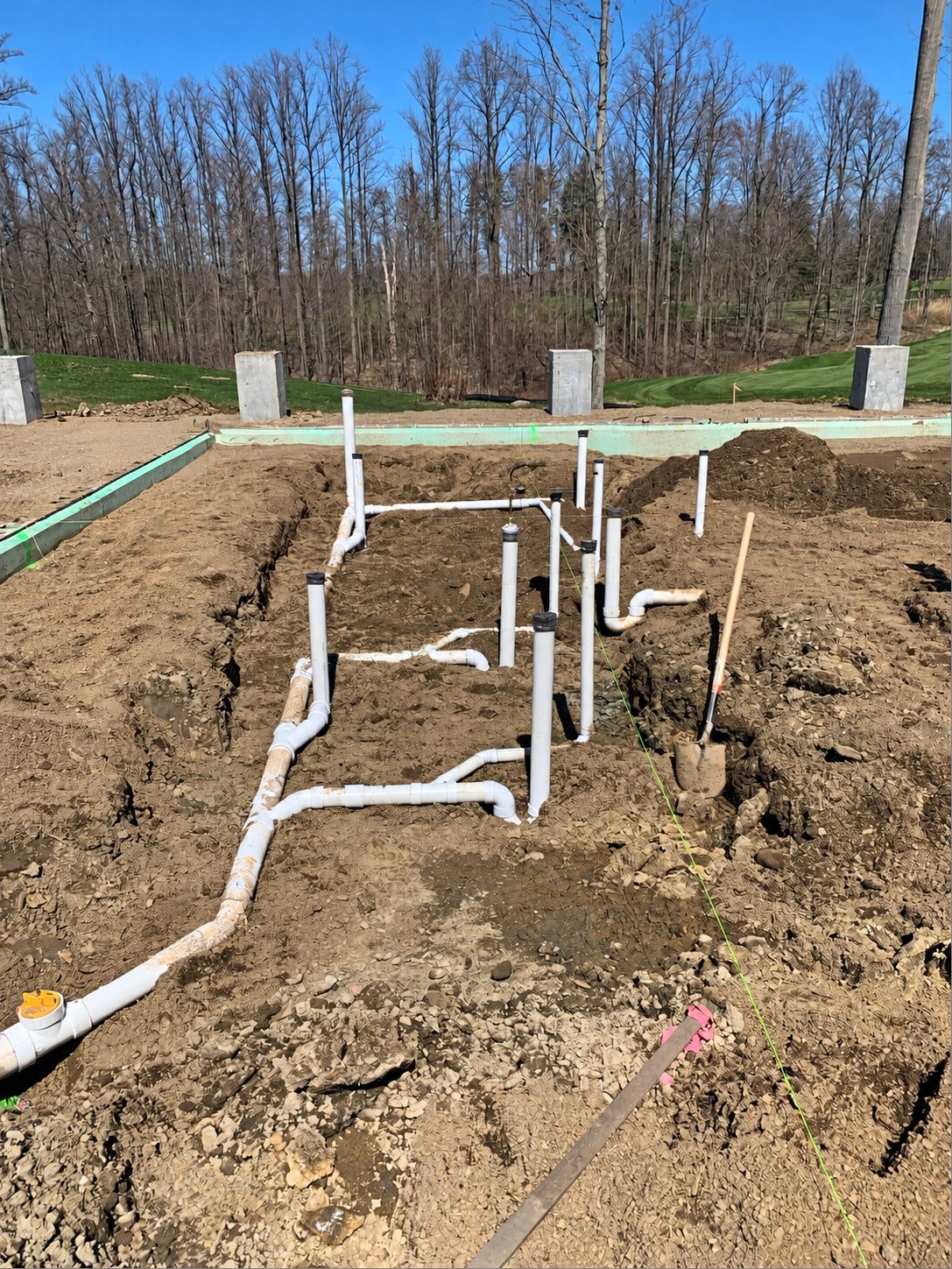Underground plumbing rough-in for a new home: white PVC drain lines and risers laid in the dirt inside the foundation