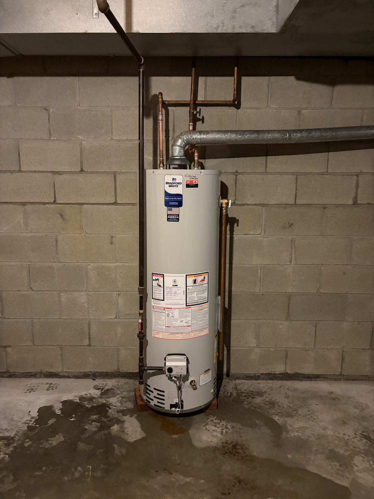 A new Bradford White gas water heater installed against a block basement wall with new copper water lines and venting